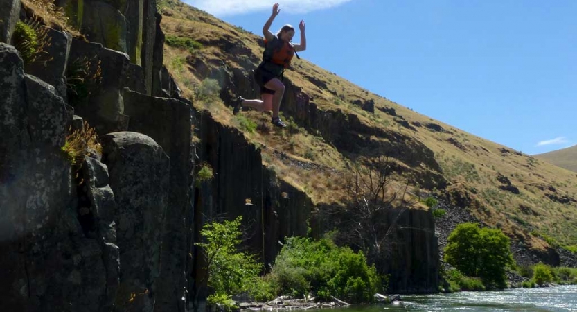 a person wearing a life jacket is in mid-air after jumping off a rock face into the water